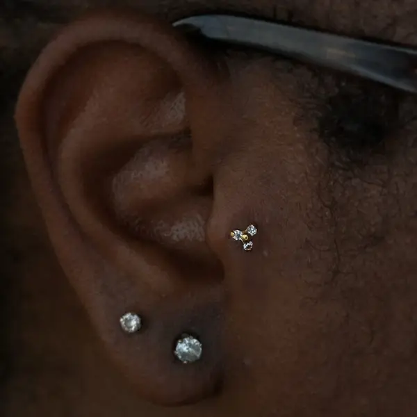 Tragus piercing with a gold three-bead trinity cluster and gemstone lobe studs by T (Piercing Piranha) at Modified Tattoo Gallery in Winter Park, FL