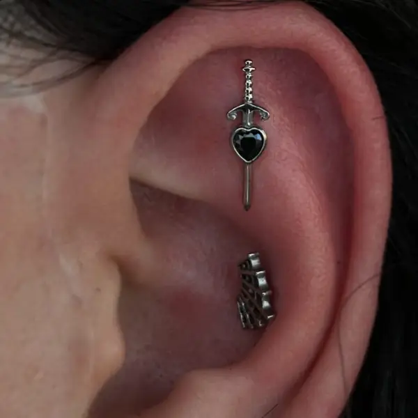 Rook piercing with a dagger charm and a conch piercing with an ornate huggie by T (Piercing Piranha) at Modified Tattoo Gallery in Winter Park, FL