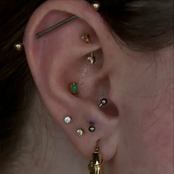 Fully curated ear with an industrial barbell, helix, conch with a green jade gem, tragus, and stacked lobe piercings by T (Piercing Piranha) at Modified Tattoo Gallery in Winter Park, FL