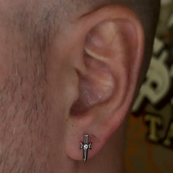 Earlobe piercing with a silver dagger charm by T (Piercing Piranha) at Modified Tattoo Gallery in Winter Park, FL
